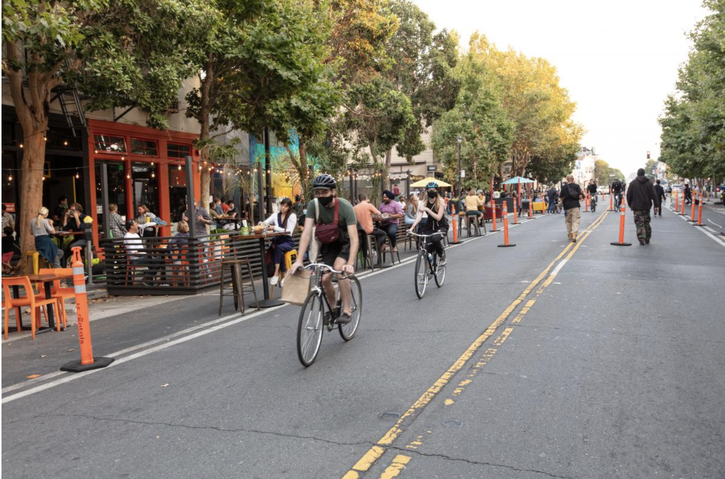 Protected bike lane with cyclists riding alongside outdoor dining on a San Francisco street